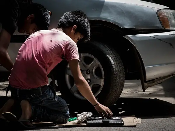 Niño trabajando en arreglo de autos - Día Mundial contra el Trabajo Infantil